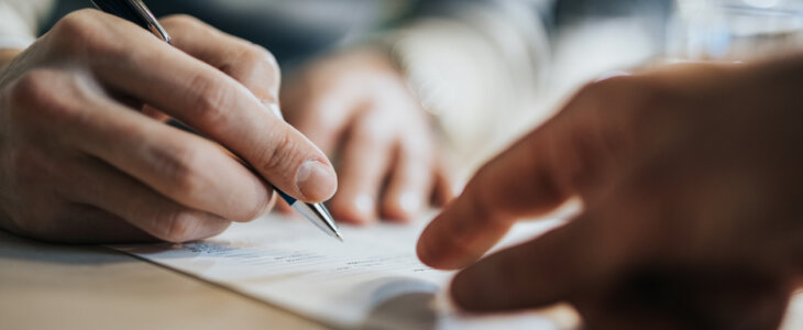 Close up picture of a man signing a piece of paper with a pen